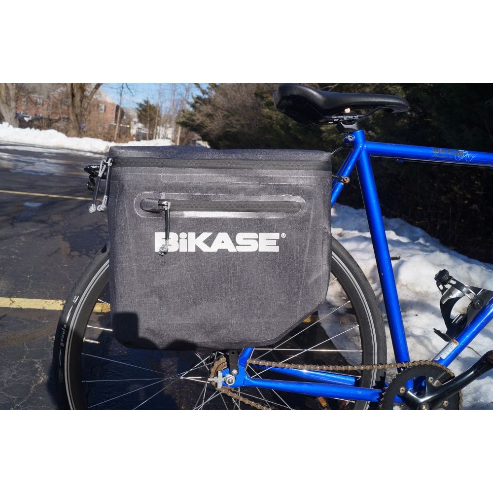 Blue bicycle with a gray Hikase bag attached to the rear wheel on a snowy street.